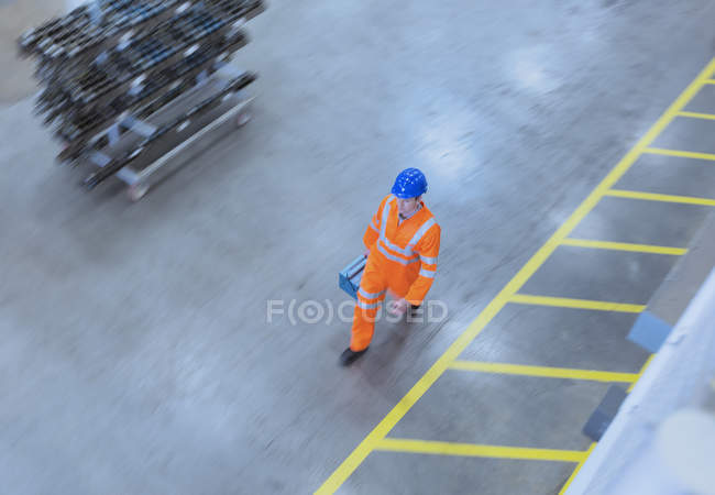 Lavoratore in abbigliamento riflettente che cammina con cassetta degli attrezzi in fabbrica — Foto stock