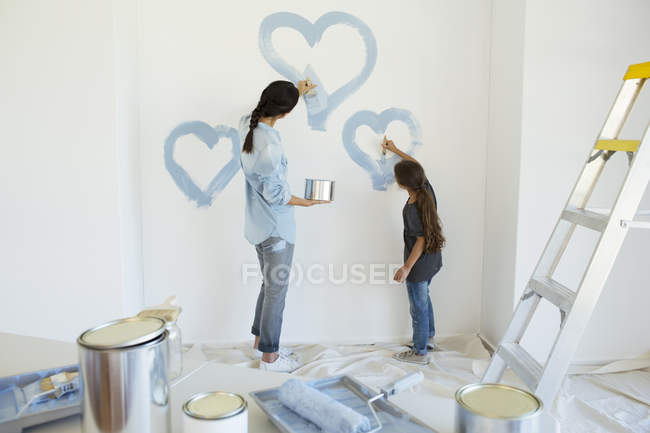 Madre e figlia che dipingono cuori blu sul muro in una nuova casa — Foto stock