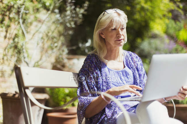 Seniorin benutzt Laptop auf sonniger Gartenbank — Stockfoto
