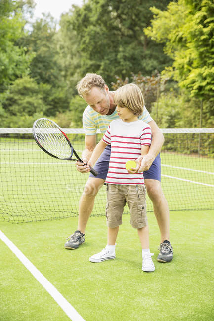 Padre enseñando hijo a jugar tenis en la cancha de hierba - foto de stock