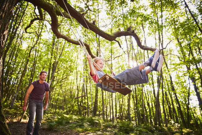 Отец толкает дочь на веревке качели в лесу — стоковое фото