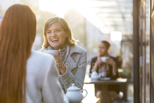 Mujeres riendo y bebiendo té en la cafetería de la acera - foto de stock