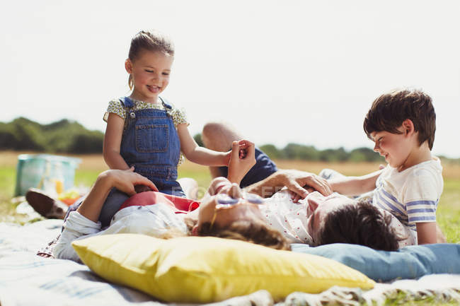 Family relaxing on blanket in sunny field — Stock Photo