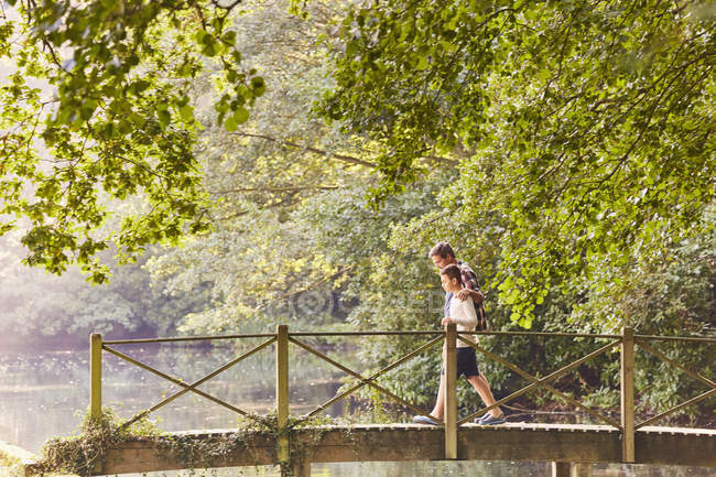 Pai e filho atravessando passarela no parque com árvores — Fotografia de Stock