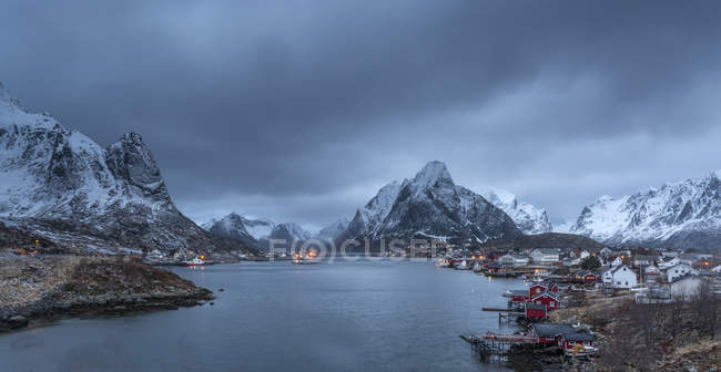 Заснеженный горный хребет над рыбацкой деревней в сумерках, Ринг, Лофские острова, Норвегия — стоковое фото