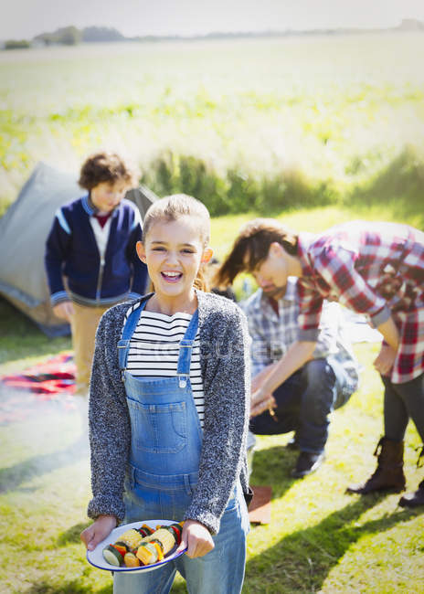 Portrait smiling girl with vegetable skewers at sunny campsite — Stock Photo