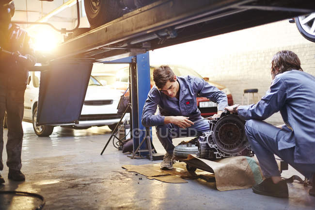 Mecánica examinando parte en taller de reparación de automóviles - foto de stock