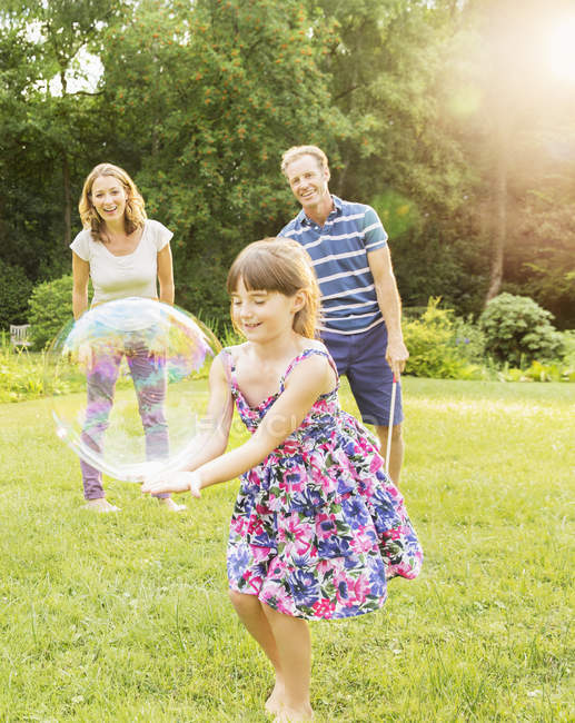 Familia feliz jugando con burbujas en el patio trasero - foto de stock