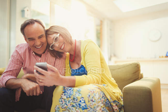 Lächelndes älteres Paar beim SMS-Schreiben mit Handy im Wohnzimmer — Stockfoto