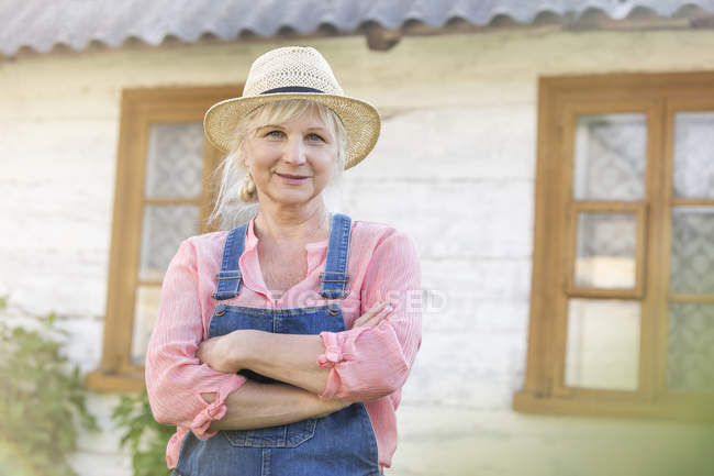Portrait smiling farmer in overalls and straw hat outside farmhouse — Stock Photo