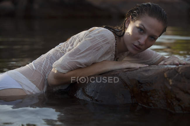 Portrait of sensual woman laying on rock in river — Stock Photo