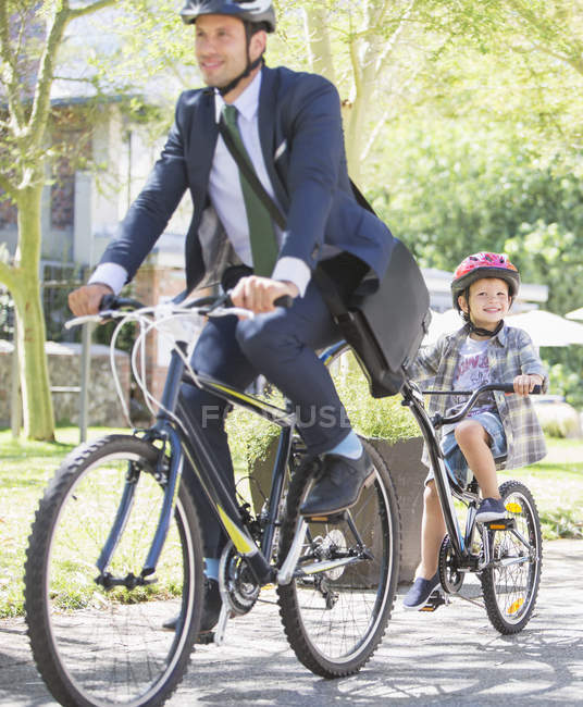 Businessman in suit and helmet riding tandem bicycle with son — Stock Photo