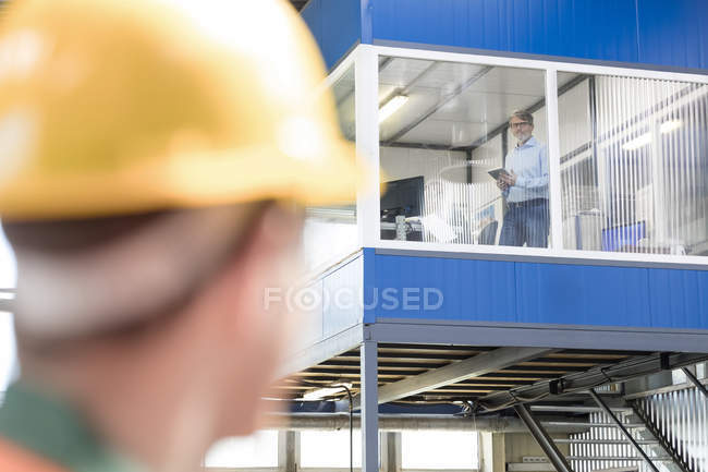 Ouvrier regardant vers le haut à l'homme d'affaires dans le bureau d'usine — Photo de stock