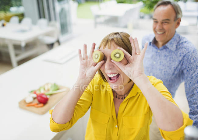 Porträt verspielte reife Frau, die Augen mit Kiwi-Scheiben bedeckt — Stockfoto