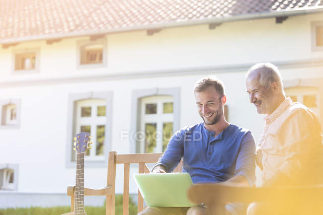 Father and adult son using laptop on garden bench — Stock Photo