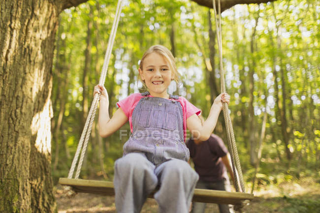 Retrato sorridente menina balançando na corda balançar na floresta — Fotografia de Stock