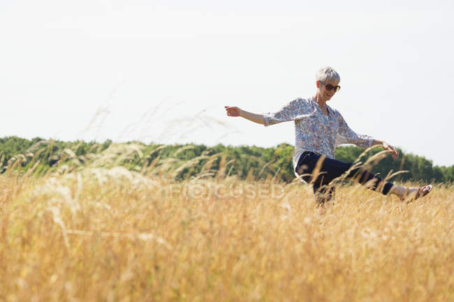 Игривая пожилая женщина танцует на солнечном поле — стоковое фото