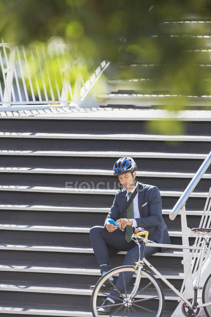 Homme d'affaires avec casque et textos de vélo avec téléphone portable sur les escaliers urbains — Photo de stock