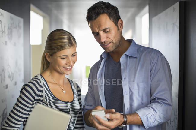 Business people looking down at cell phone in corridor — Stock Photo