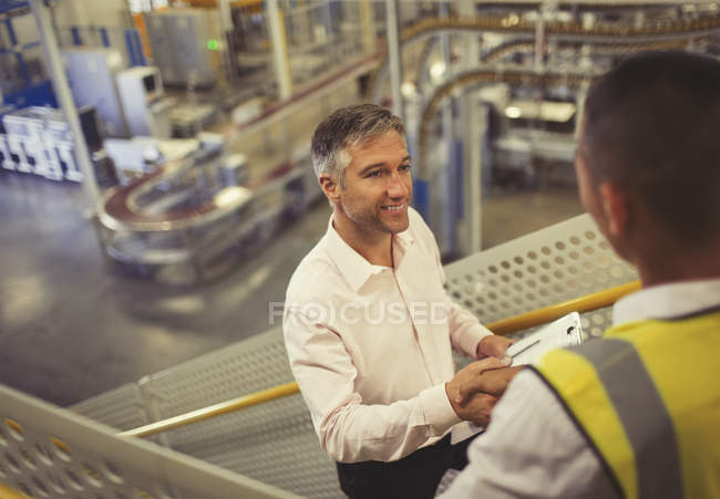 Supervisor y trabajador apretón de manos en fábrica - foto de stock