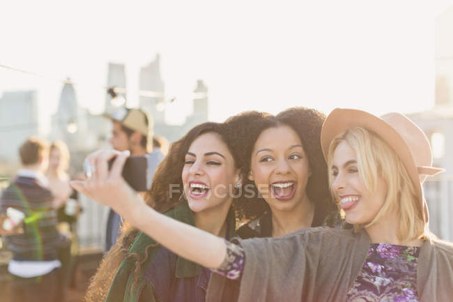 Enthusiastic young women taking selfie at rooftop party — Stock Photo