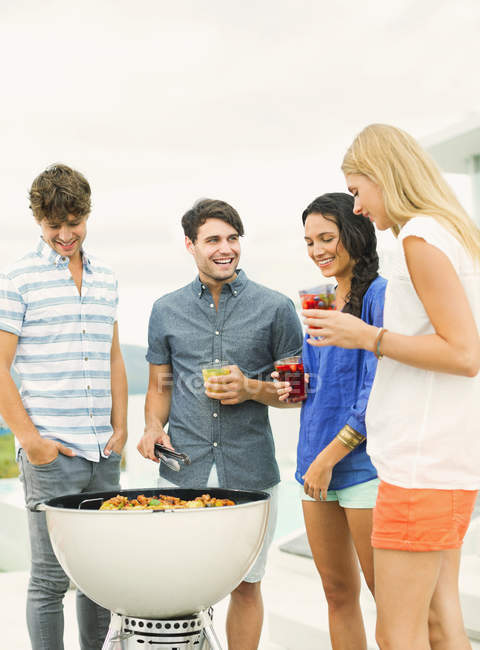 Giovani amici parlando intorno barbecue — Foto stock