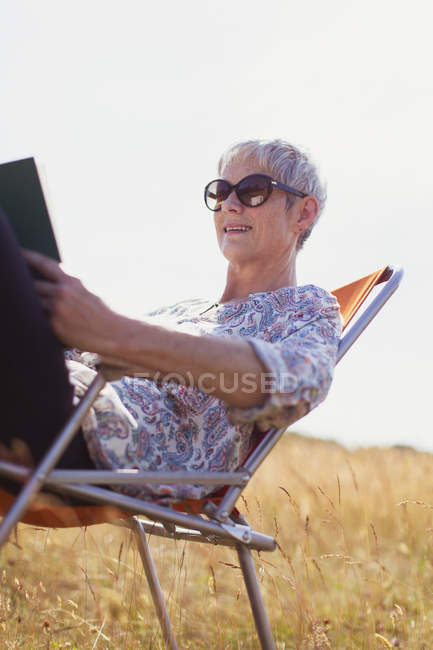 Senior livre de lecture femme dans le domaine ensoleillé — Photo de stock