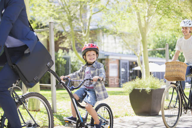 Retrato niño sonriente en casco montar en bicicleta tándem con padre en el parque - foto de stock