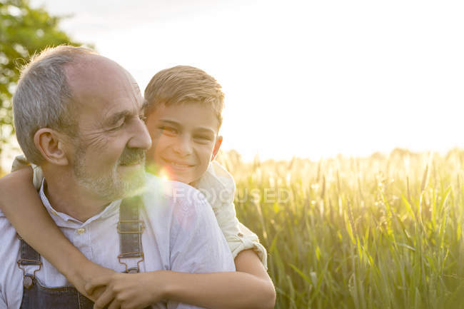 Portrait affectionate grandson hugging grandfather in rural wheat field — Stock Photo