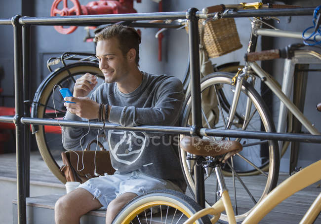 Hombre joven mensajes de texto con el teléfono celular cerca de bicicletas en la barandilla - foto de stock