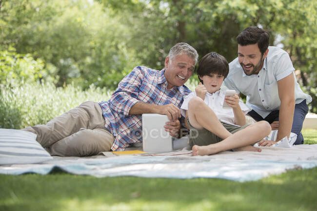 Mehrgenerationenmänner mit Handy auf Decke im Gras — Stockfoto