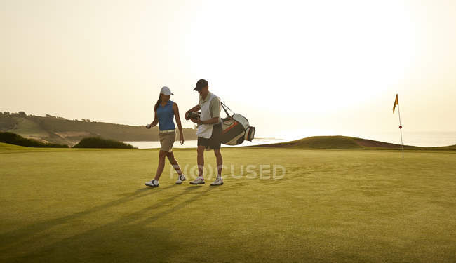 Caddy and woman walking on golf course overlooking ocean — Stock Photo