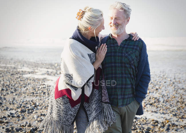 Senior couple hugging and walking on sunny rocky beach — Stock Photo