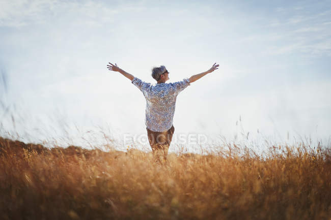 Exuberant senior woman with arms outstretched in sunny field — Stock Photo