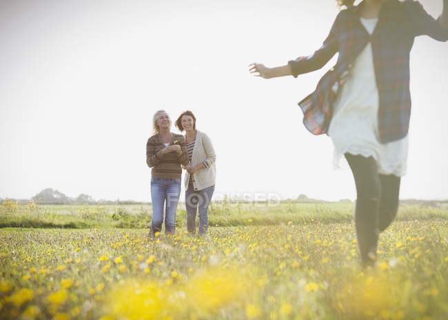 Жінки спостерігають, як дівчина біжить на сонячному лузі з дикими квітами — стокове фото