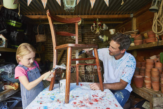 Father and daughter painting chair in workshop — Stock Photo