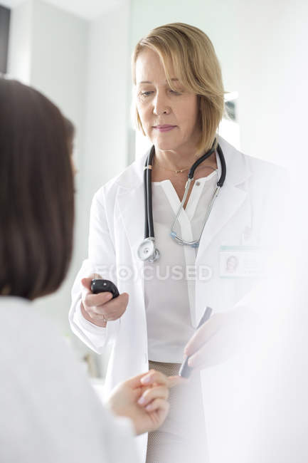Médico que examina el azúcar en sangre del paciente para la diabetes en sala de examen - foto de stock