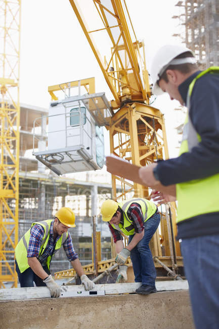 Construction Workers Using Level Tool Below Crane At Construction Site 