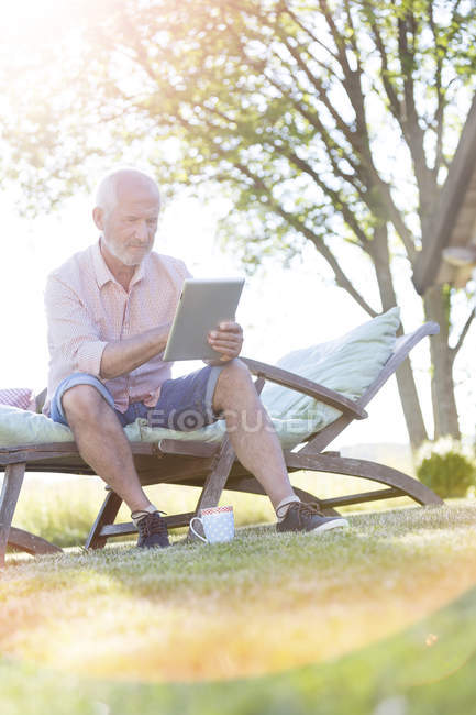 Uomo anziano che utilizza tablet digitale sulla sedia a sdraio in cortile — Foto stock