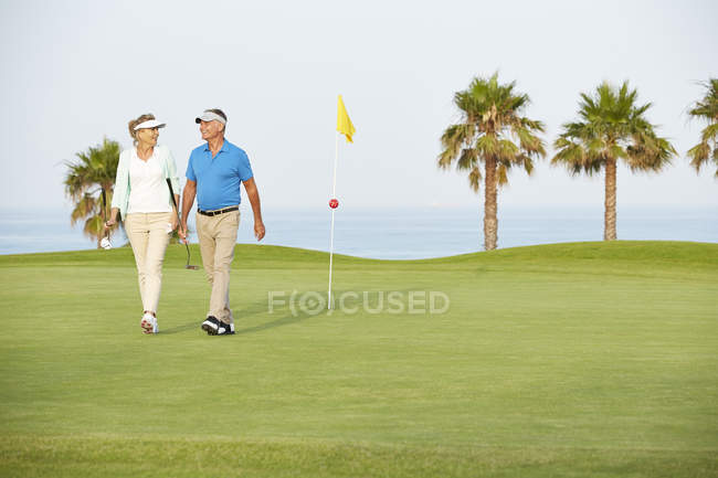Старшая пара, идущая по полю для гольфа — стоковое фото