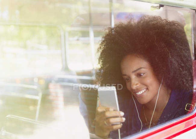 Donna sorridente con afro ascoltare musica con cuffie e lettore mp3 sul bus — Foto stock