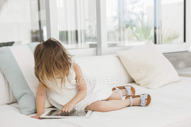 Тоддлер девушка с помощью цифрового планшета на диване — стоковое фото