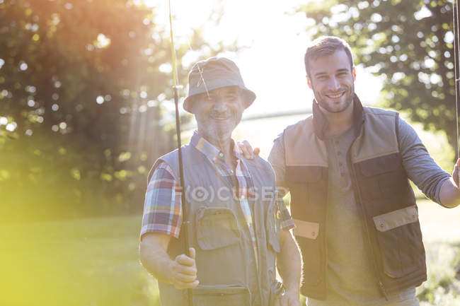 Portrait smiling father and adult son with fishing rods — Stock Photo