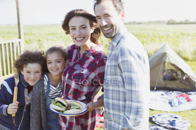 Портрет улыбающейся семьи с барбекю гамбургеров в солнечном кемпинге — стоковое фото