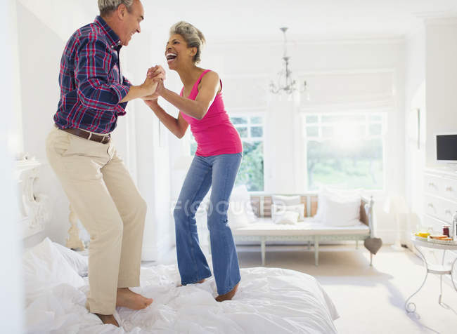 Playful mature couple jumping on top of bed — Stock Photo
