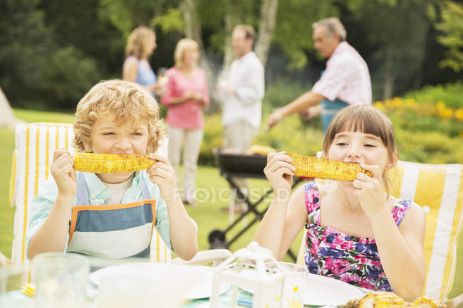 Niños felices comiendo en la mesa en el patio trasero - foto de stock