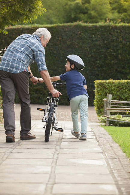 Grand-père et petit-fils poussant le vélo sur le trottoir — Photo de stock