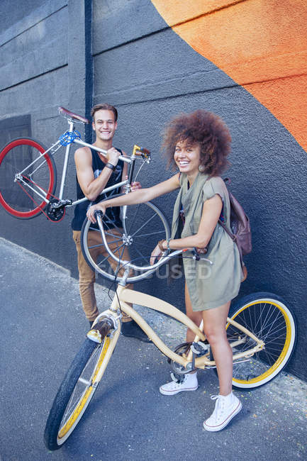 Portrait amis souriants avec des vélos à côté du mur urbain — Photo de stock