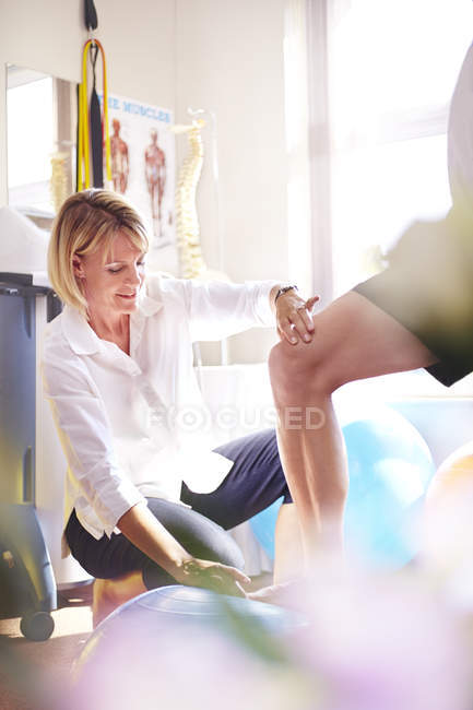 Physiothérapeute guidant le genou de l'homme marchant sur la balle de fitness — Photo de stock