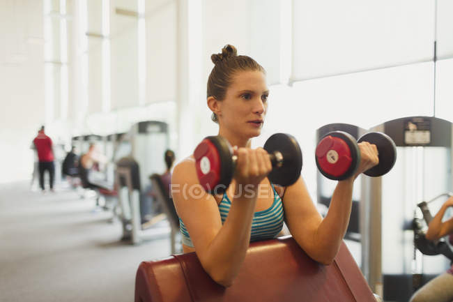 Mulher focada fazendo halteres bíceps cachos no ginásio — Fotografia de Stock